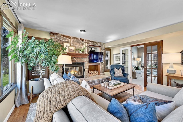 living area featuring wood finished floors, a stone fireplace, french doors, and baseboards