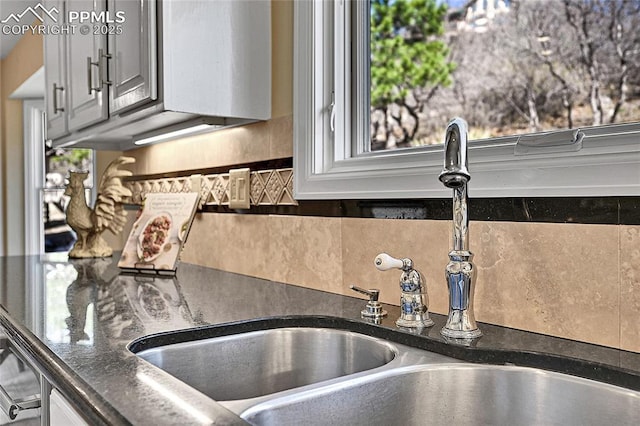 kitchen view of a sink, tasteful backsplash, and dark countertops