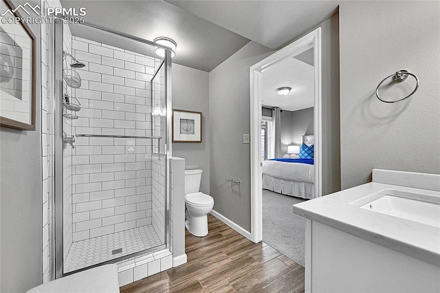 ensuite bathroom with wood finished floors, a stall shower, toilet, vanity, and baseboards