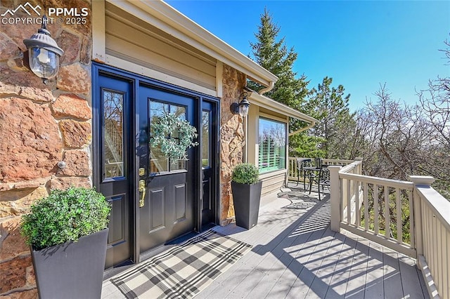 property entrance featuring stone siding, a wooden deck, and outdoor dining space