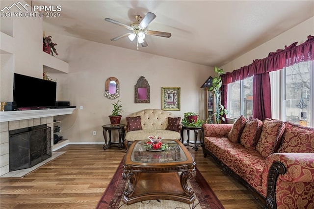 living area with a fireplace, wood finished floors, lofted ceiling, baseboards, and ceiling fan