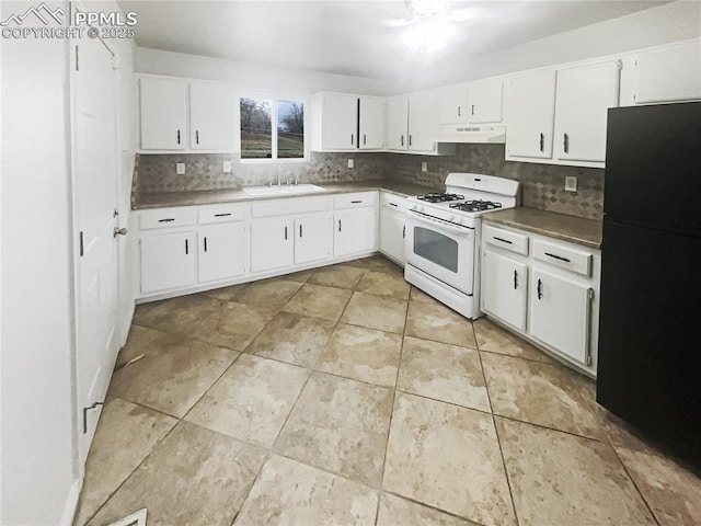 kitchen featuring white gas range, under cabinet range hood, decorative backsplash, a sink, and freestanding refrigerator
