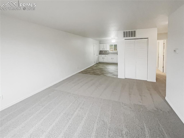 unfurnished living room with baseboards, visible vents, and light colored carpet