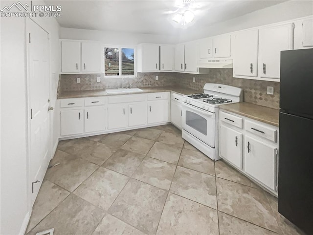 kitchen with under cabinet range hood, backsplash, a sink, freestanding refrigerator, and white range with gas cooktop
