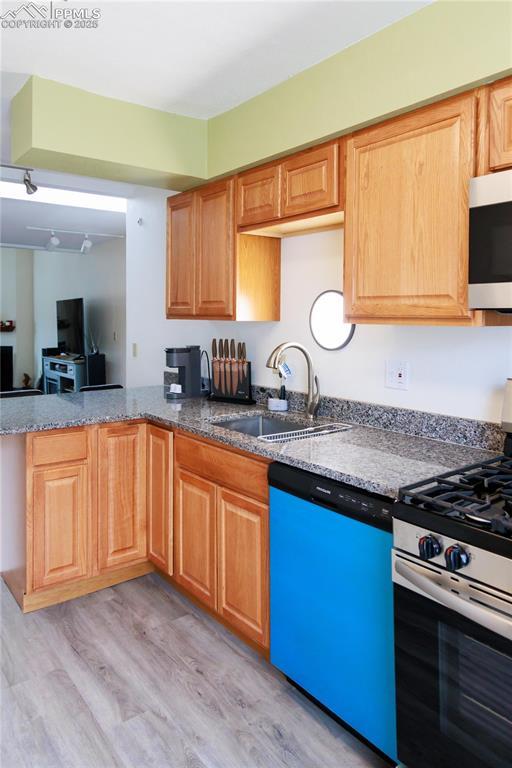 kitchen featuring light wood-type flooring, gas range, a sink, dishwashing machine, and a peninsula