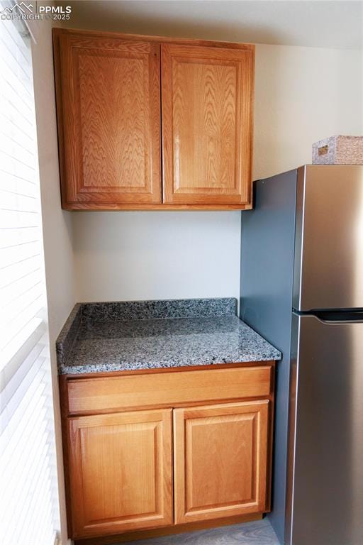 kitchen with freestanding refrigerator, dark stone counters, and brown cabinetry