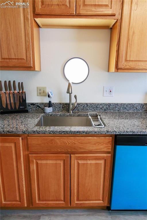 kitchen with dark stone countertops, a sink, brown cabinets, and dishwasher