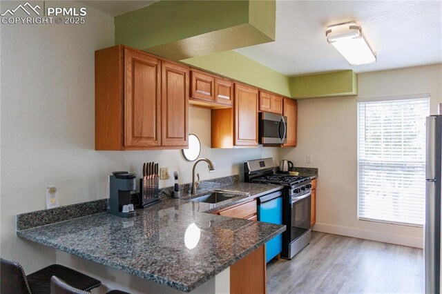 kitchen with a sink, a kitchen bar, a peninsula, stainless steel appliances, and dark stone counters