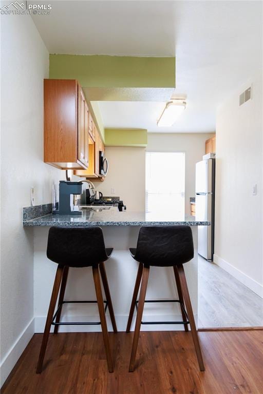 kitchen with visible vents, a peninsula, a kitchen breakfast bar, and freestanding refrigerator