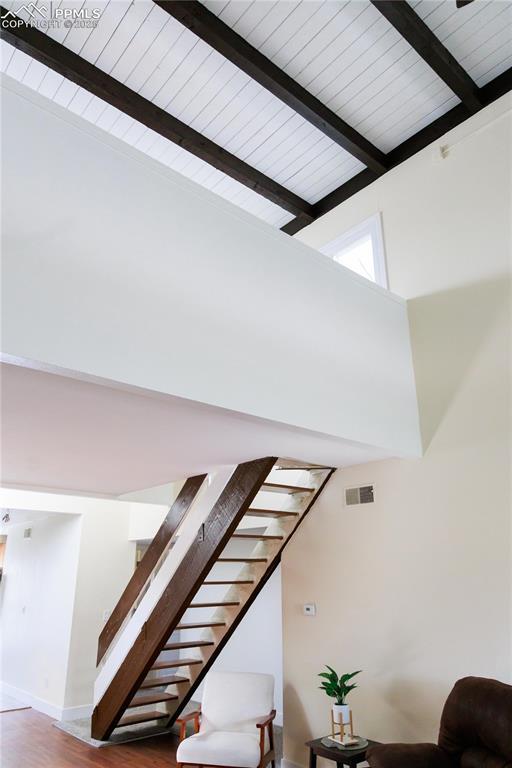 staircase featuring wood finished floors, a towering ceiling, beam ceiling, and visible vents