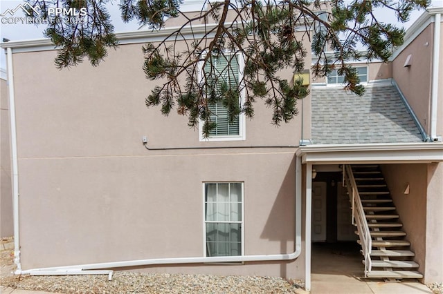 view of side of home featuring stucco siding, a shingled roof, and stairway