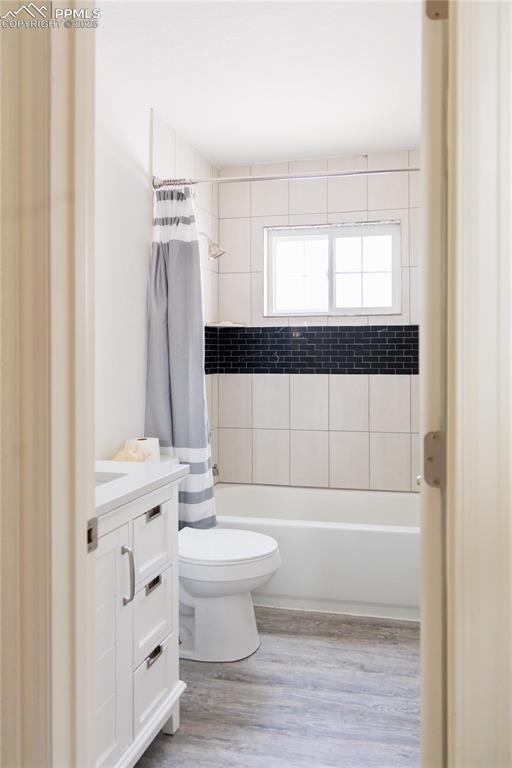 full bath with shower / bathtub combination with curtain, wood finished floors, toilet, and vanity