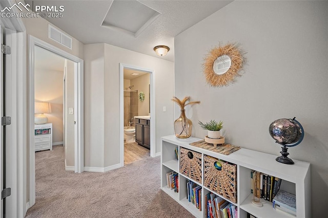 hallway with visible vents, attic access, baseboards, and light carpet