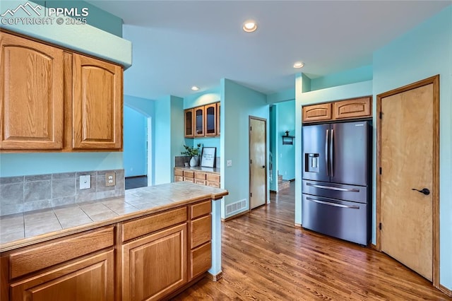 kitchen with stainless steel fridge, tile counters, visible vents, glass insert cabinets, and wood finished floors