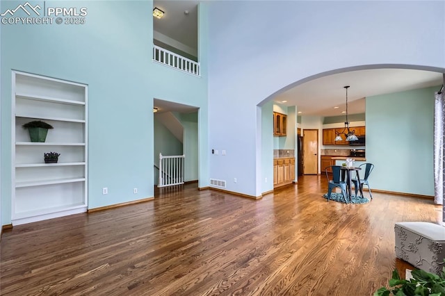 unfurnished living room with baseboards, visible vents, arched walkways, and dark wood-type flooring