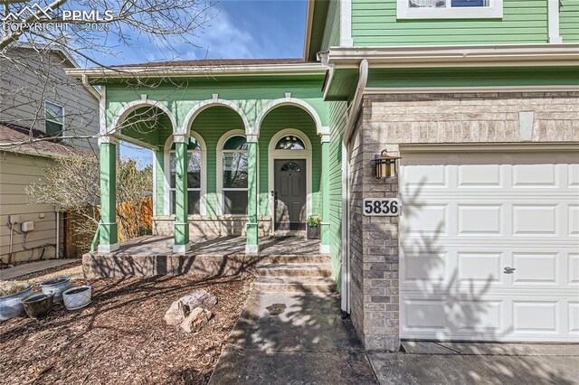 entrance to property with stone siding, covered porch, and a garage