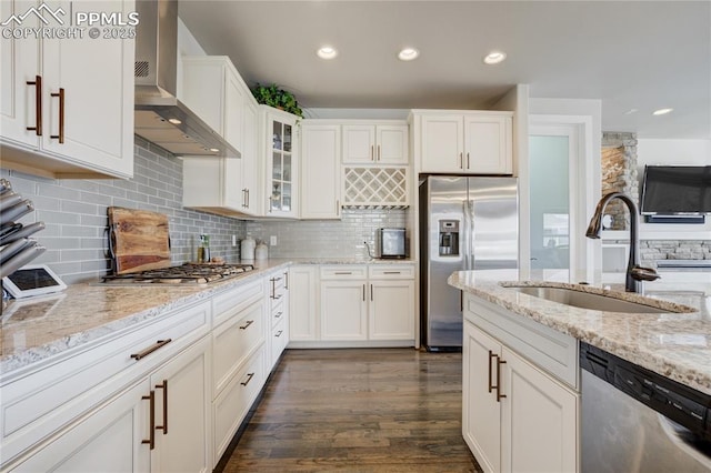 kitchen with dark wood-style flooring, white cabinetry, wall chimney exhaust hood, appliances with stainless steel finishes, and a sink