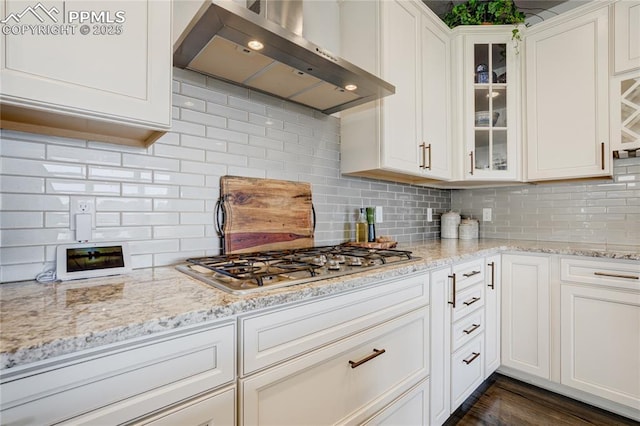kitchen featuring stainless steel gas cooktop, glass insert cabinets, wall chimney exhaust hood, and light stone counters