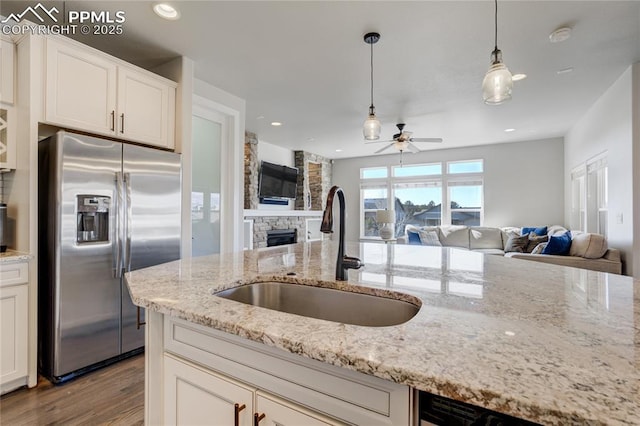 kitchen with stainless steel fridge with ice dispenser, open floor plan, a stone fireplace, and a sink