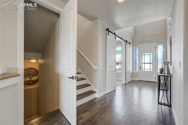 entryway with dark wood-type flooring, baseboards, stairway, and a barn door