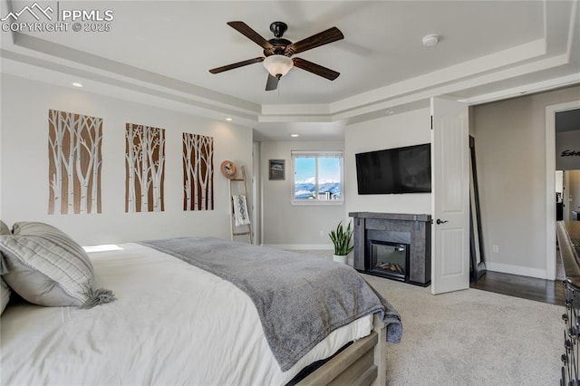 bedroom with a glass covered fireplace, recessed lighting, baseboards, and a raised ceiling