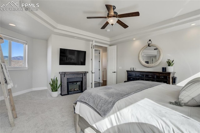 carpeted bedroom featuring ceiling fan, a glass covered fireplace, recessed lighting, a raised ceiling, and baseboards