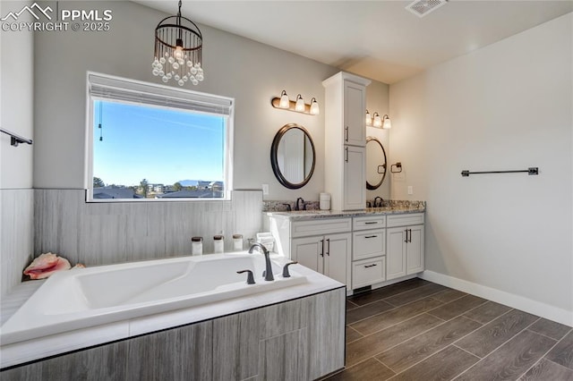 bathroom featuring visible vents, a sink, double vanity, wood finish floors, and a garden tub