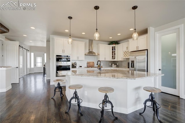 kitchen featuring baseboards, wall chimney exhaust hood, dark wood finished floors, stainless steel appliances, and backsplash
