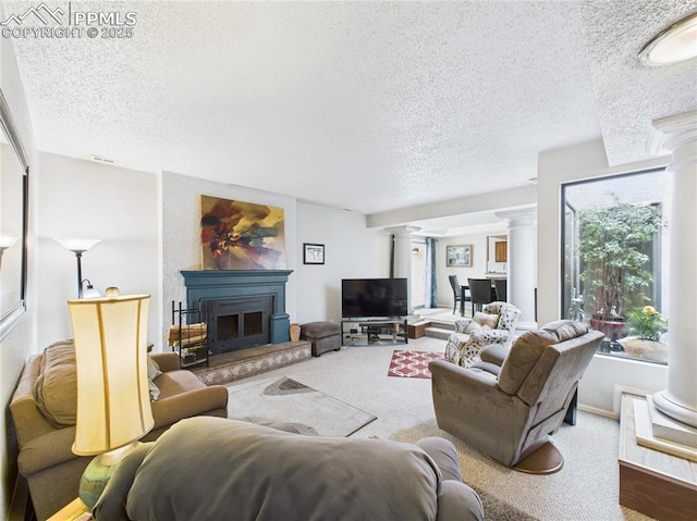 living room featuring decorative columns, a fireplace with raised hearth, carpet flooring, and a textured ceiling