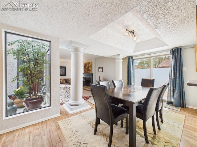 dining area with light wood finished floors, decorative columns, a raised ceiling, and a textured ceiling