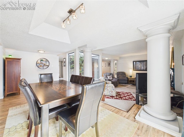 dining room featuring decorative columns, a tray ceiling, light wood finished floors, and a textured ceiling
