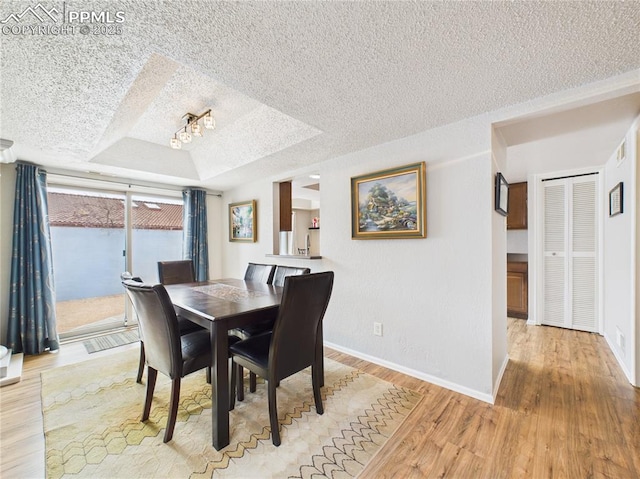 dining room featuring a tray ceiling, baseboards, light wood finished floors, and a textured ceiling