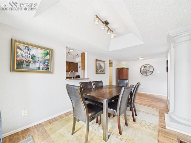 dining space featuring baseboards, a textured ceiling, light wood-style floors, and decorative columns