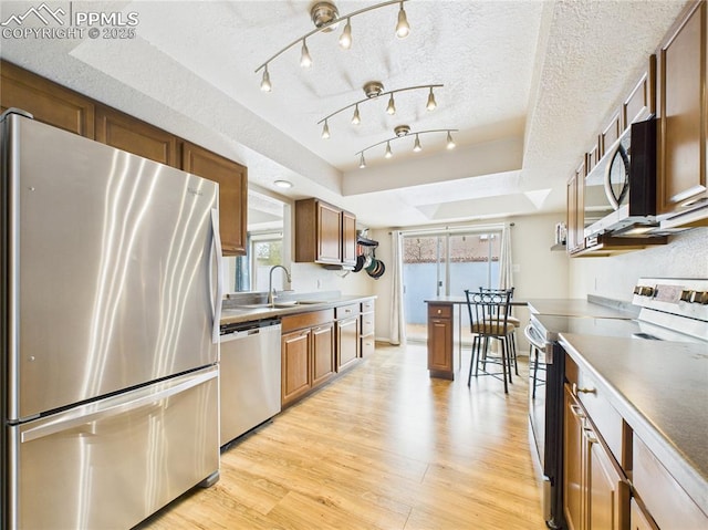 kitchen featuring a tray ceiling, a sink, a textured ceiling, light wood-type flooring, and stainless steel appliances