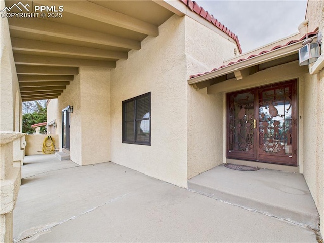 property entrance with stucco siding, a tiled roof, and a patio area