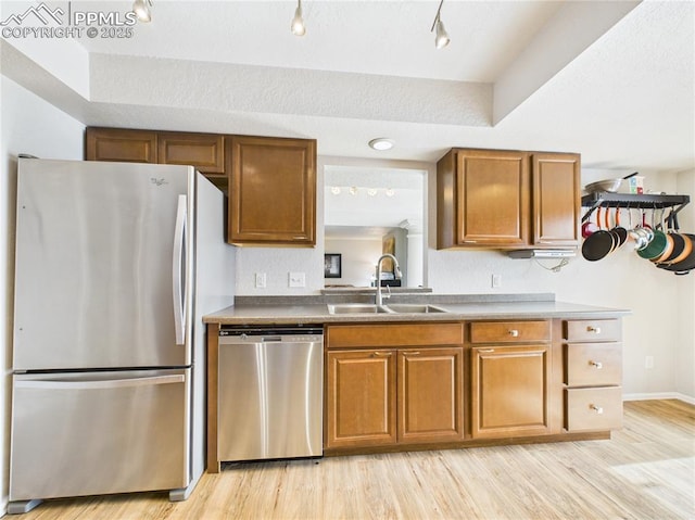 kitchen with a sink, appliances with stainless steel finishes, light wood-style floors, and brown cabinets