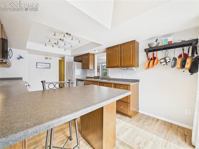 kitchen featuring freestanding refrigerator, a raised ceiling, a kitchen bar, brown cabinets, and visible vents