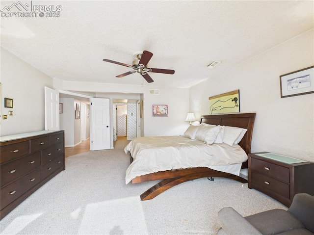 bedroom with light carpet, a textured ceiling, visible vents, and a ceiling fan