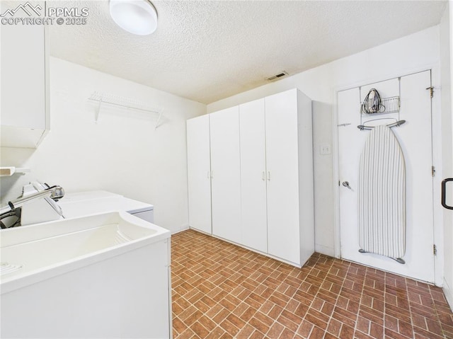 clothes washing area featuring a textured ceiling, visible vents, laundry area, brick patterned floor, and a sink