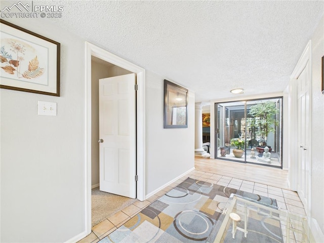 hallway featuring baseboards, decorative columns, light tile patterned floors, and a textured ceiling