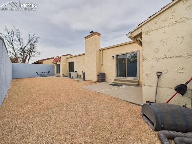 rear view of house with stucco siding, central air condition unit, a fenced backyard, and a patio area
