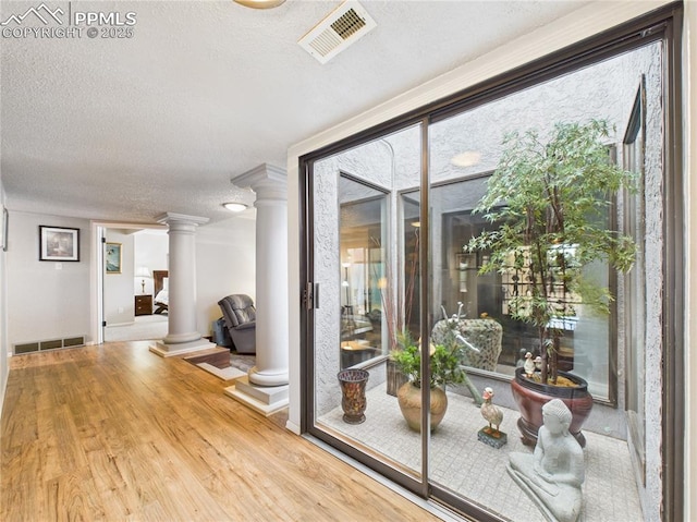 interior space with ornate columns, a textured ceiling, visible vents, and wood finished floors