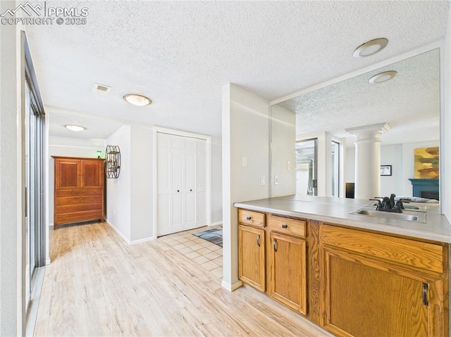 kitchen featuring light countertops, a sink, a textured ceiling, light wood-type flooring, and brown cabinetry