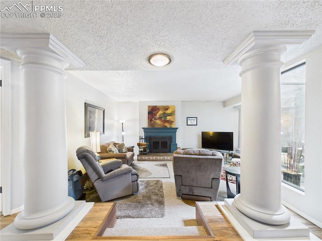 living area featuring decorative columns, wood finished floors, a fireplace with raised hearth, and a textured ceiling