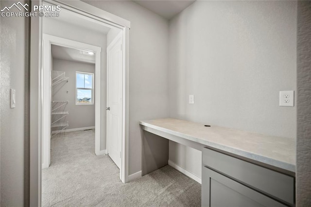unfurnished office with baseboards, built in desk, and light carpet