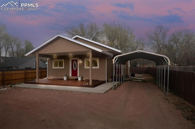 view of front of house featuring stucco siding, a detached carport, covered porch, and fence