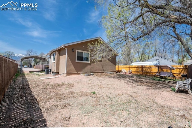 back of house featuring a carport, a fenced backyard, central AC unit, and stucco siding