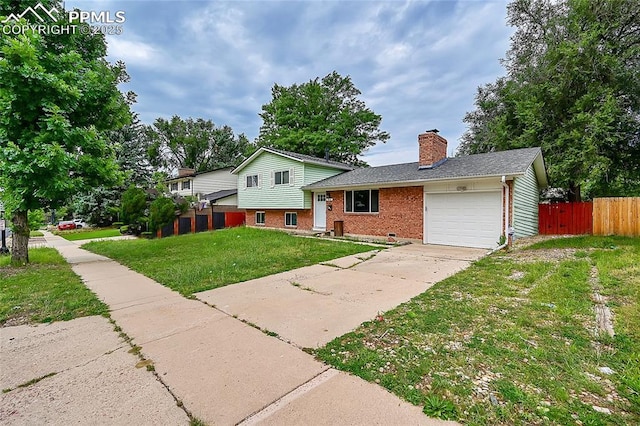 tri-level home featuring fence, an attached garage, a chimney, a front yard, and brick siding