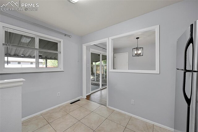unfurnished room featuring an inviting chandelier, light tile patterned floors, visible vents, and a wealth of natural light
