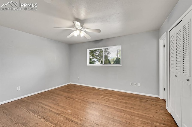 unfurnished bedroom with a closet, wood finished floors, baseboards, visible vents, and ceiling fan